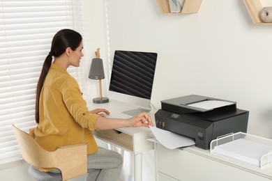 Woman using modern printer at workplace indoors