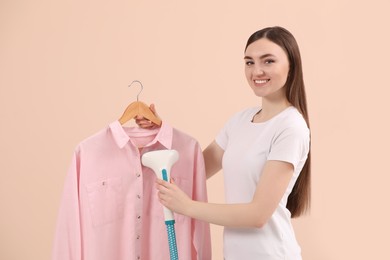 Woman steaming shirt on hanger against beige background