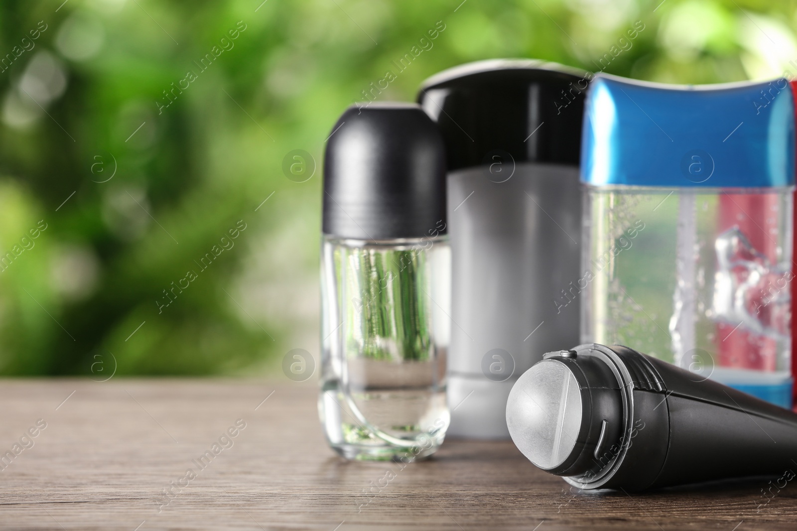 Photo of Different deodorants on wooden table against blurred background. Space for text