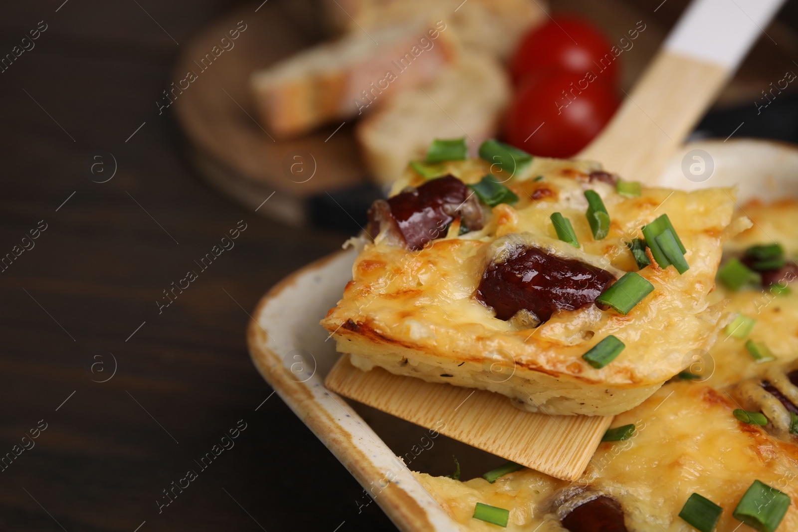 Photo of Taking piece of tasty sausage casserole from baking dish at table, closeup. Space for text