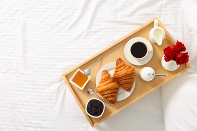 Photo of Tasty breakfast served in bed. Fresh croissants, coffee, honey and jam on wooden tray, space for text