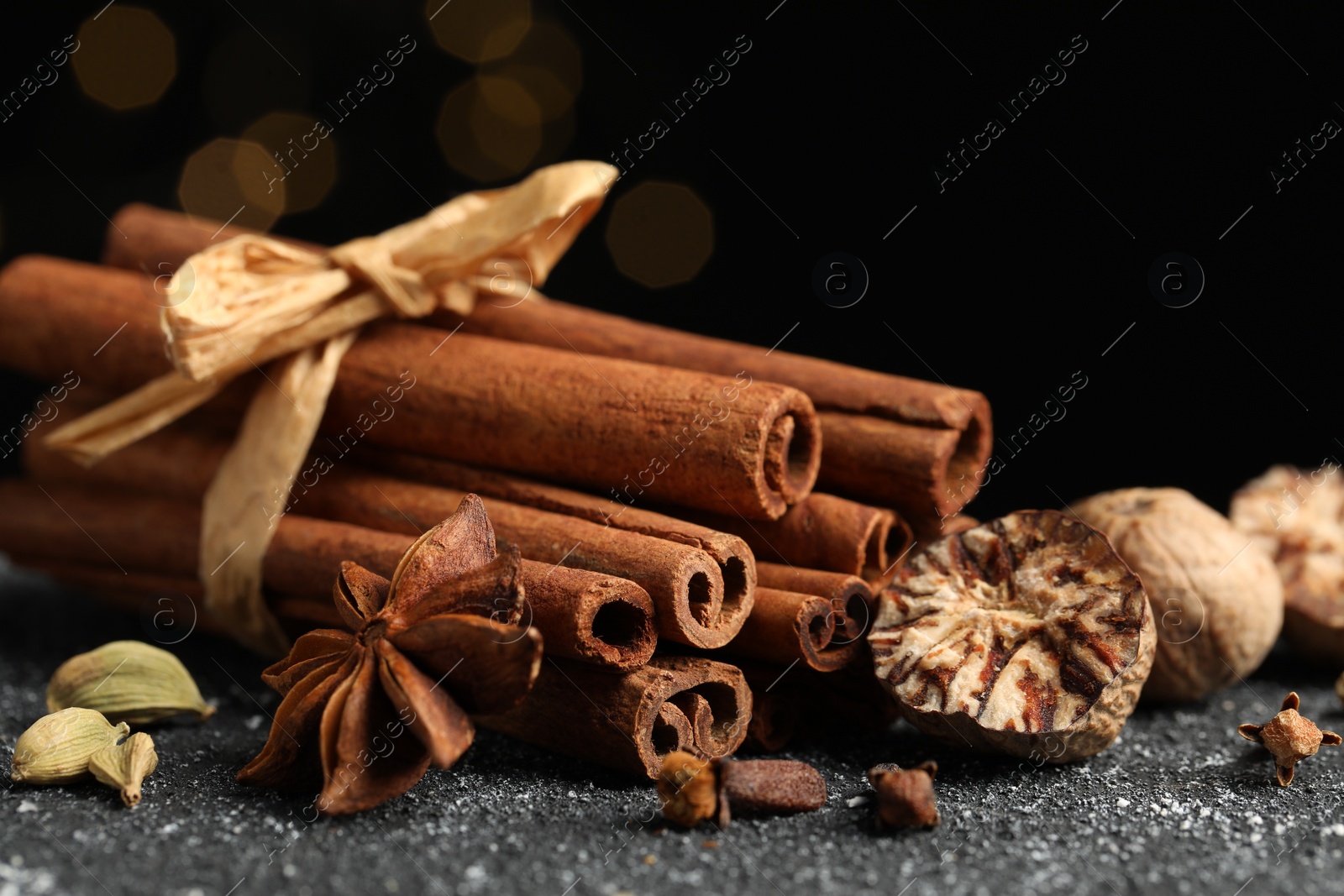 Photo of Different aromatic spices on grey textured table against black background, closeup