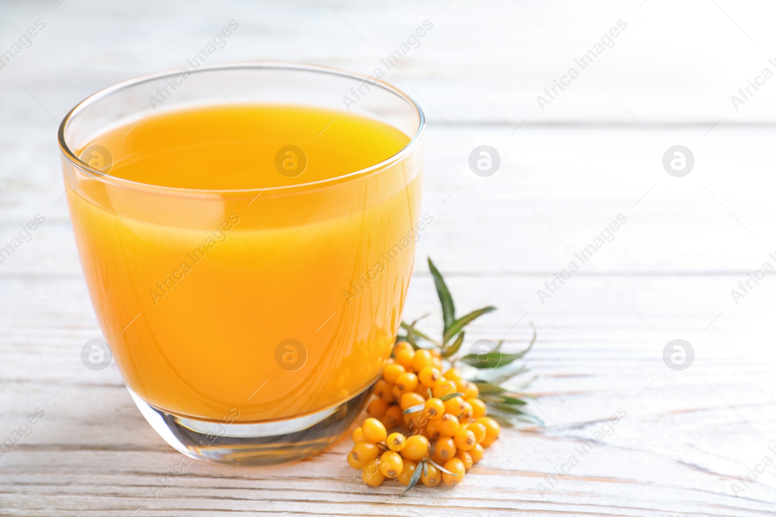 Photo of Delicious sea buckthorn juice and fresh berries on white wooden table, closeup. Space for text