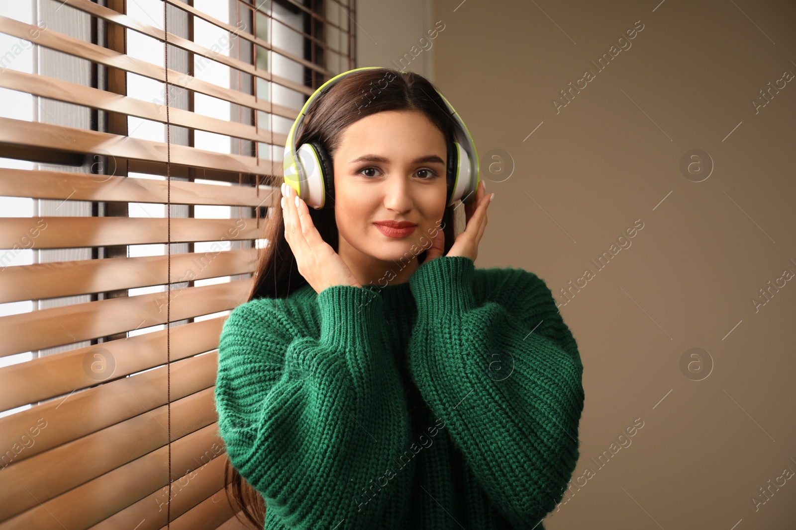 Photo of Young woman listening to audiobook near window indoors