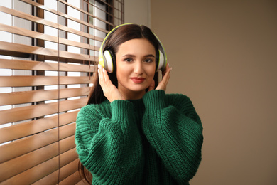 Young woman listening to audiobook near window indoors