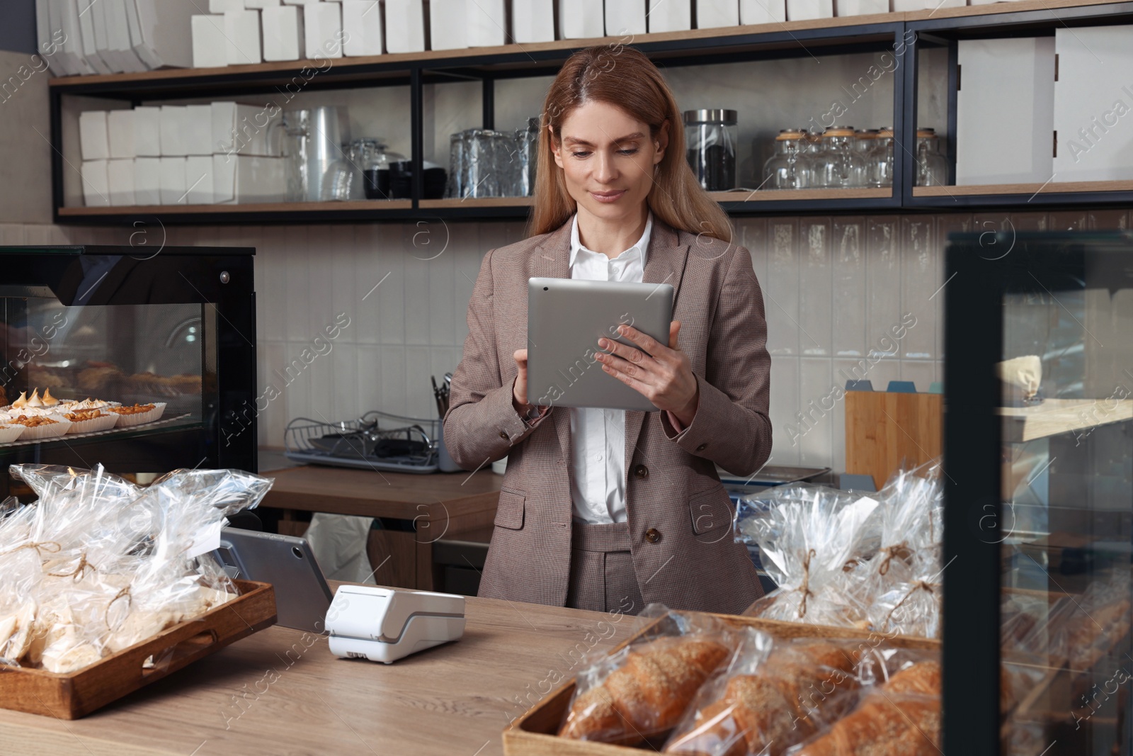 Photo of Smiling business owner with tablet at cashier desk in bakery shop