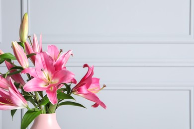 Photo of Beautiful pink lily flowers in vase against light wall, space for text