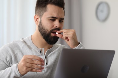 Photo of Young man taking pill against headache in office