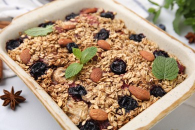 Photo of Tasty baked oatmeal with berries and almonds in baking tray on white table, closeup