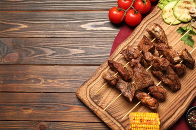 Delicious shish kebabs with vegetables and spices on wooden table, flat lay. Space for text