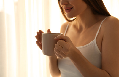 Photo of Young woman with cup near window at home, closeup. Lazy morning