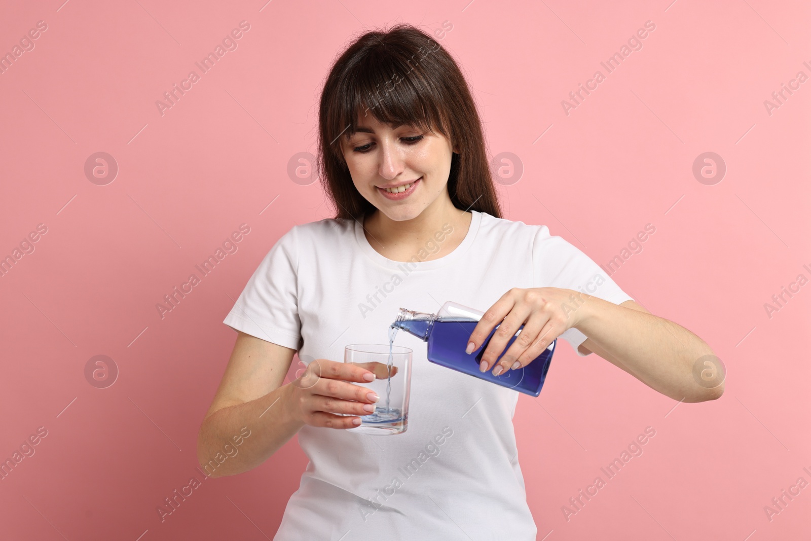 Photo of Young woman using mouthwash on pink background