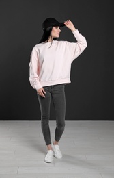 Photo of Full length portrait of young woman in sweater at black wall. Mock up for design
