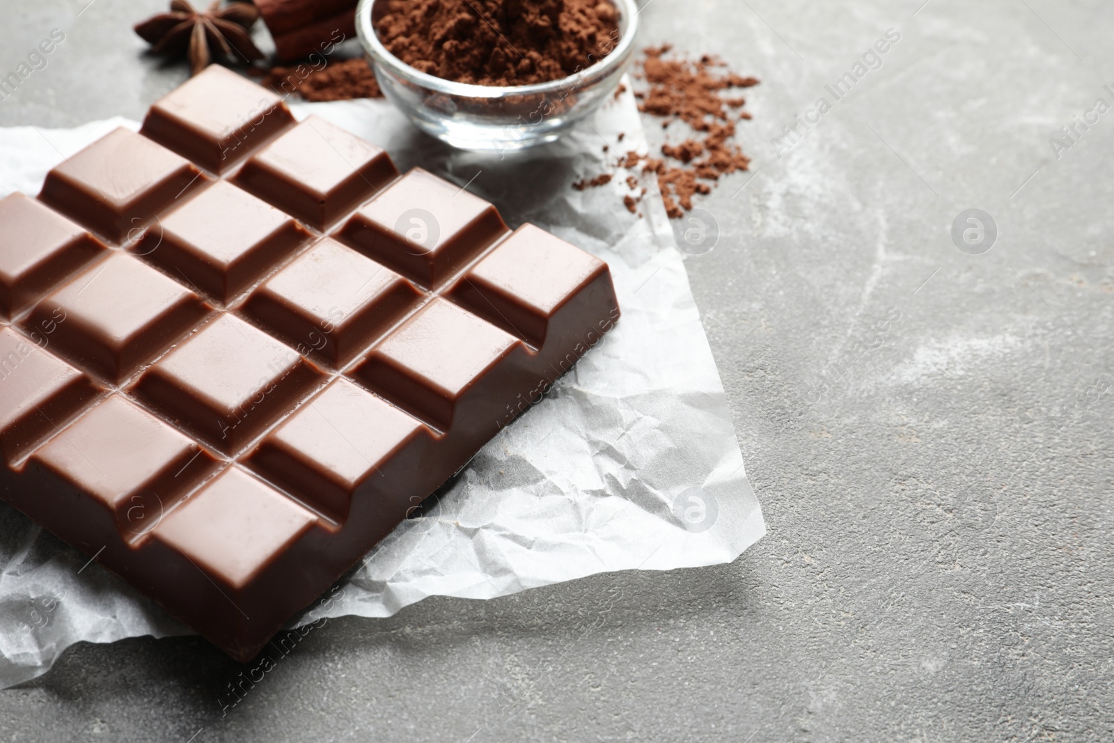 Photo of Chocolate bar and cocoa powder on grey background. Space for text