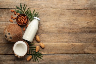 Photo of Delicious vegan milk, almonds and coconuts on wooden table, flat lay. Space for text