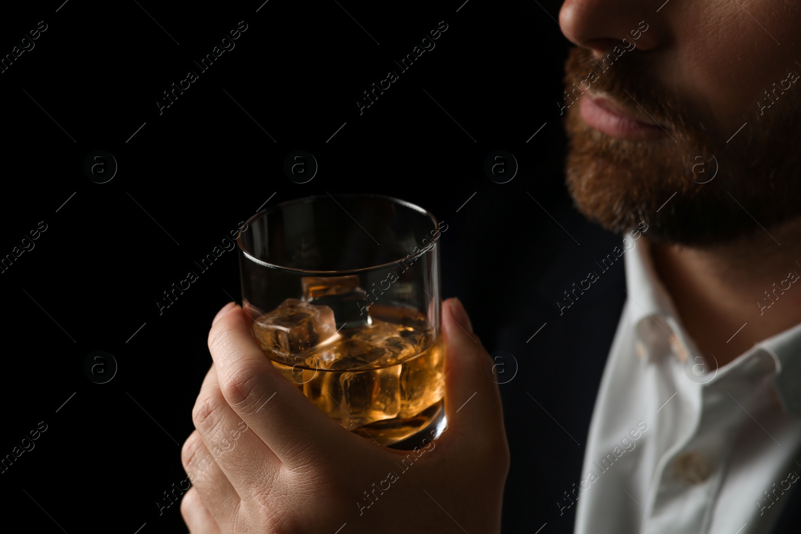 Photo of Man holding glass of whiskey with ice cubes on black background, closeup