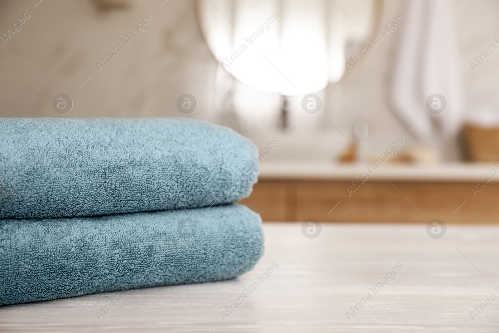 Photo of Stack of clean towels on white wooden table in bathroom. Space for text