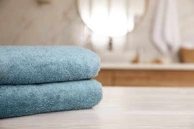 Stack of clean towels on white wooden table in bathroom. Space for text