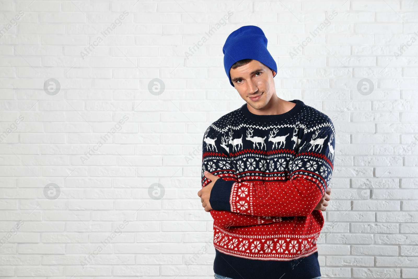 Photo of Portrait of young man in Christmas sweater and hat near white brick wall. Space for text