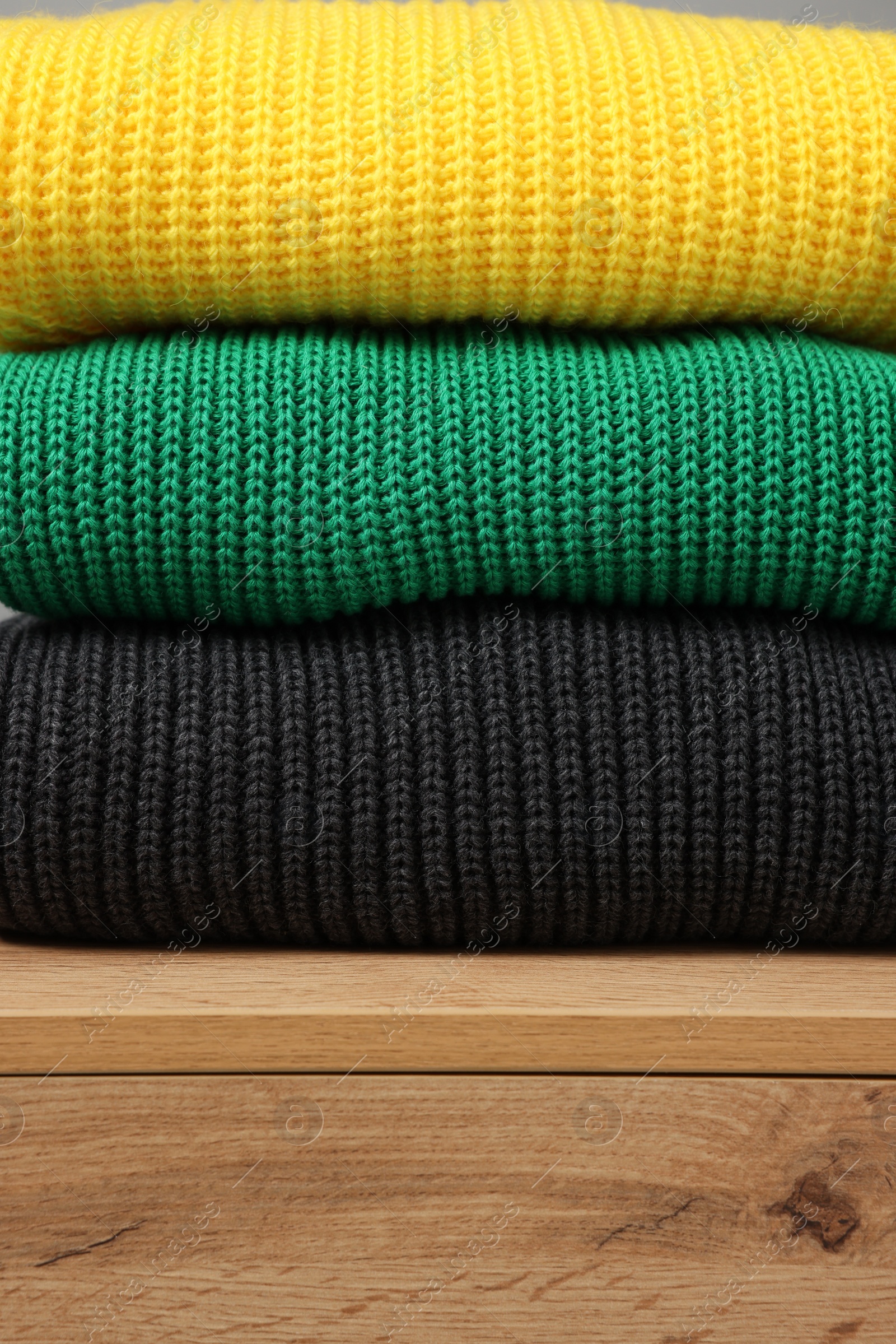 Photo of Stack of different knitted sweaters on wooden table, closeup