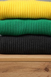 Photo of Stack of different knitted sweaters on wooden table, closeup