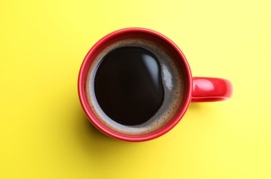 Photo of Fresh aromatic coffee in red mug on yellow background, top view