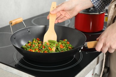 Photo of Woman cooking tasty vegetable mix in wok pan at home, closeup