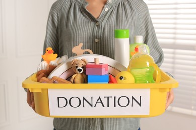 Photo of Woman holding donation box with child goods indoors, closeup