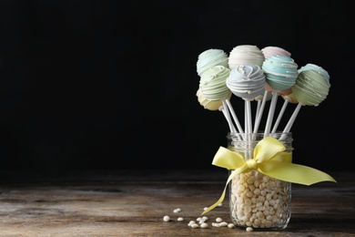 Photo of Sweet cake pops on wooden table against black background. Space for text