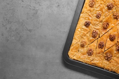 Photo of Delicious baklava with walnuts in baking pan on grey textured table, top view. Space for text
