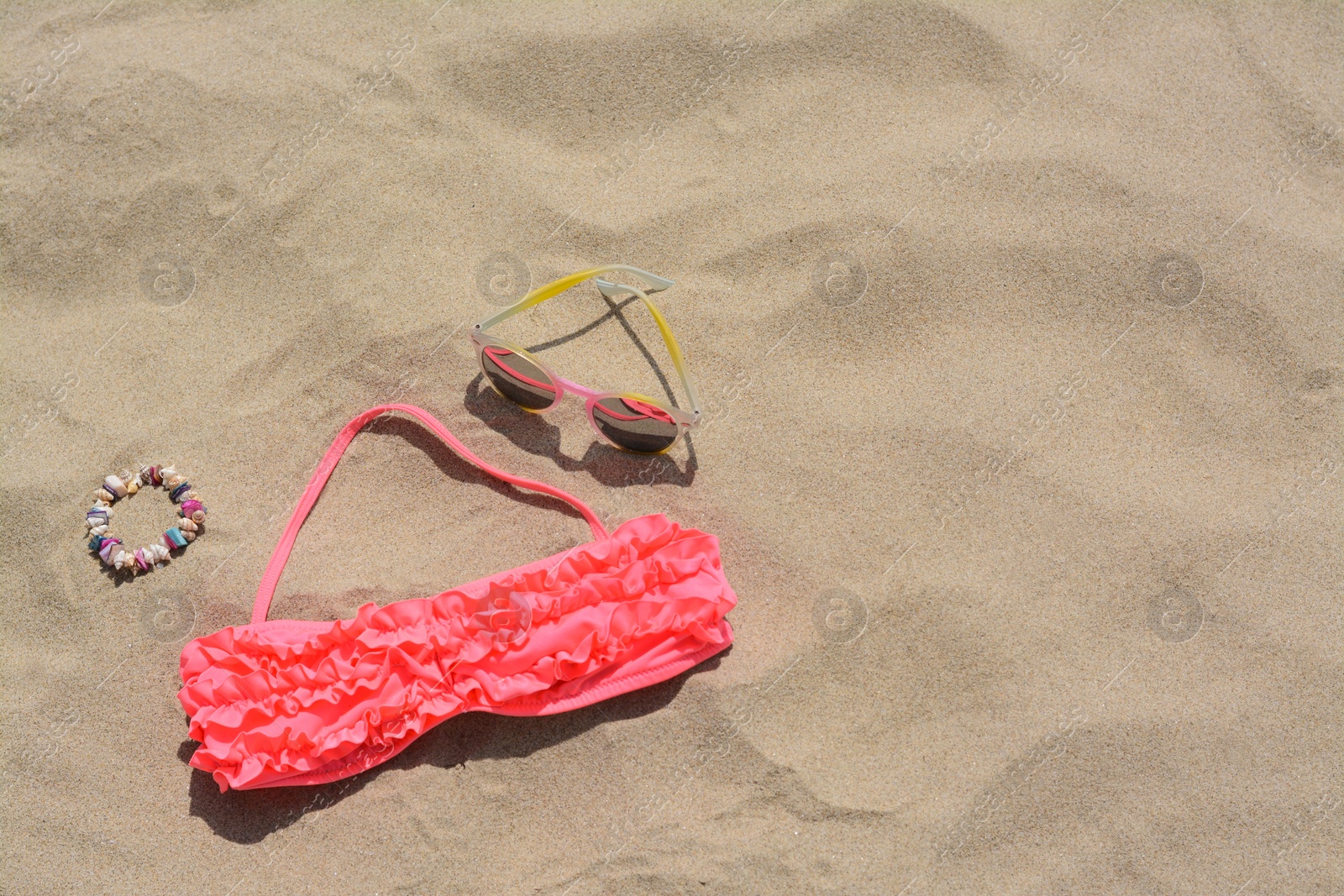 Photo of Sunglasses, bra and bracelet on sand, above view with space for text. Beach accessories