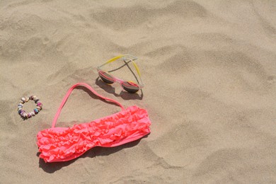 Photo of Sunglasses, bra and bracelet on sand, above view with space for text. Beach accessories