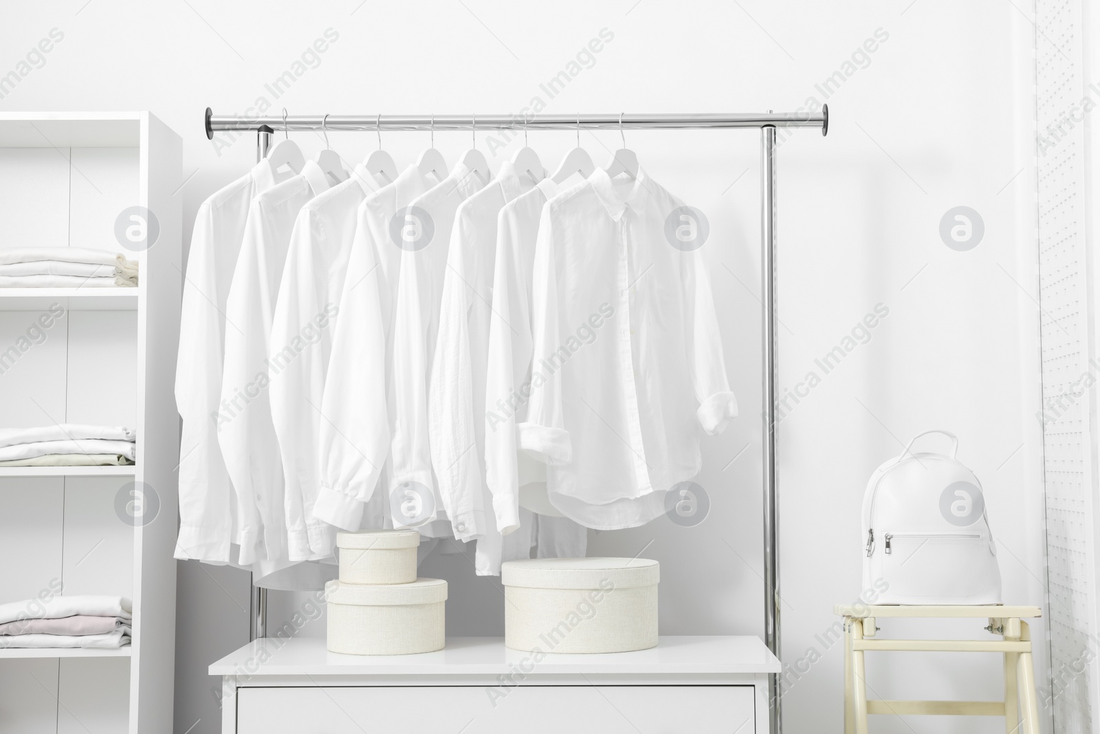 Photo of Wardrobe organization. Rack with different stylish clothes, shelving unit and folding ladder near white wall indoors