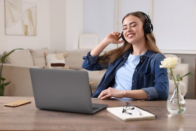 Photo of Happy woman with headphones listening to music and laptop on wooden table