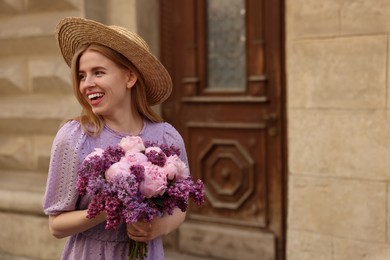 Beautiful woman with bouquet of spring flowers near building outdoors, space for text