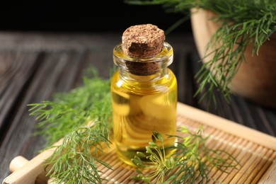 Bottle of essential oil and fresh dill on table, closeup