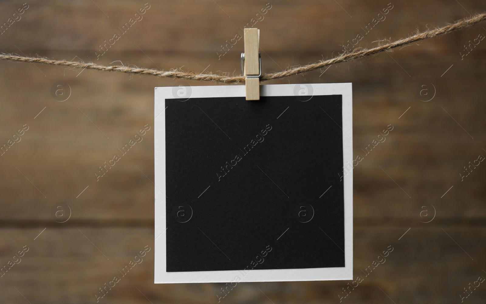 Photo of Clothespin with empty instant frame on twine against wooden background. Space for text