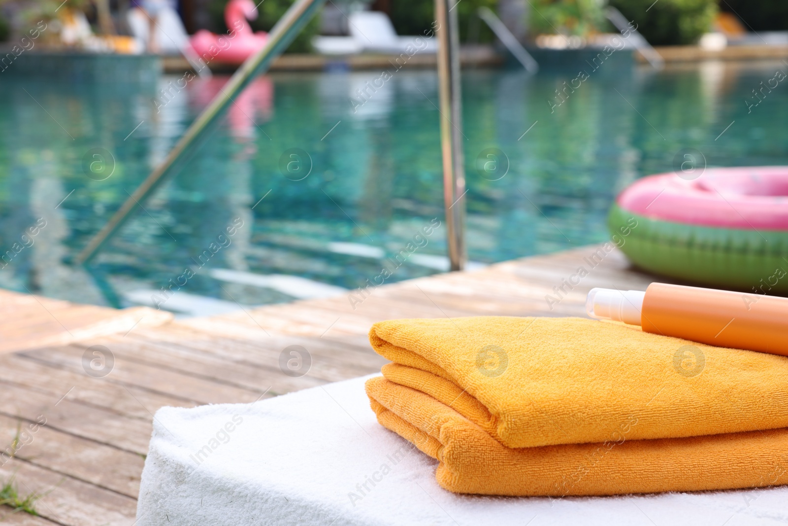 Photo of Beach towels and sunscreen on sun lounger near outdoor swimming pool at luxury resort, selective focus. Space for text