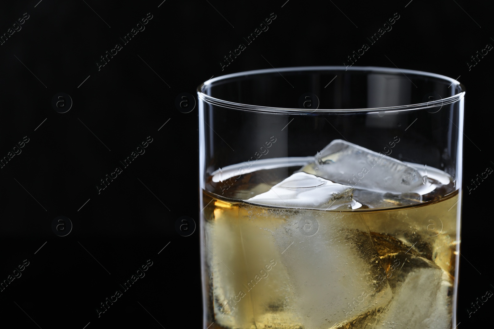 Photo of Tasty whiskey and ice cubes in glass on black background, closeup. Space for text
