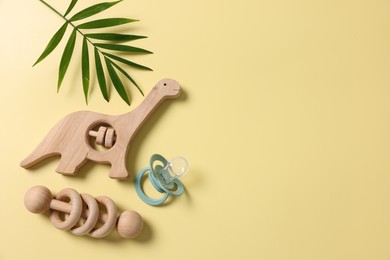 Photo of Baby accessory. Wooden rattles, pacifier and palm leaf on yellow background, flat lay. Space for text