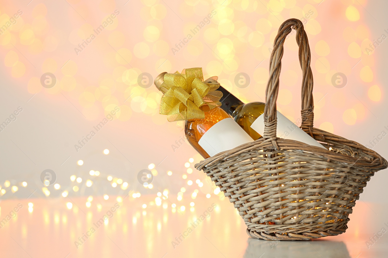 Photo of Wicker basket with bottles of wine against blurred lights. Space for text