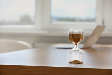 Hourglass with flowing sand on table indoors, space for text