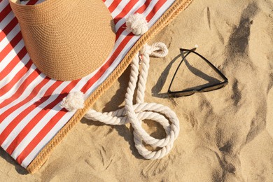 Photo of Stylish striped bag with visor cap and sunglasses on sandy beach, flat lay
