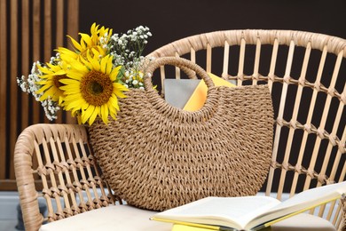 Stylish beach bag with beautiful bouquet of flowers and books on armchair indoors