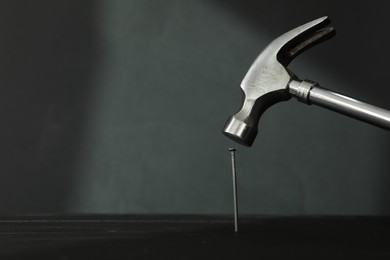 Photo of Hammering metal nail on wooden table against black background. Space for text