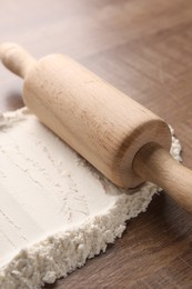 Photo of Flour and rolling pin on wooden table, closeup