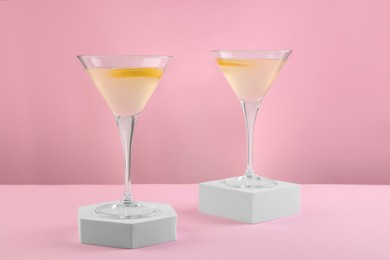Photo of Martini glasses of cocktail with lemon slices on stands against pink background