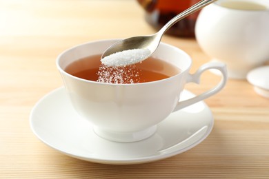 Photo of Adding sugar into cup of tea at wooden table, closeup