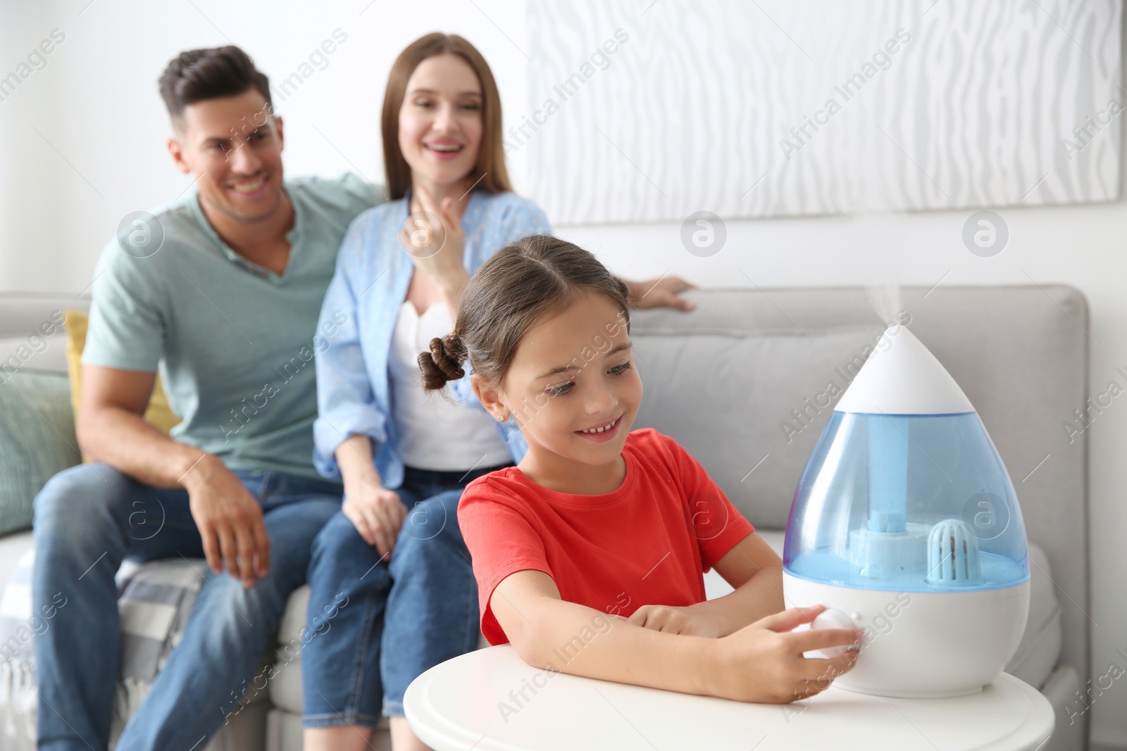 Photo of Little girl using modern air humidifier near her parents at home