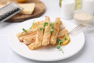 Photo of Plate with baked salsify roots and lemon on white table, closeup